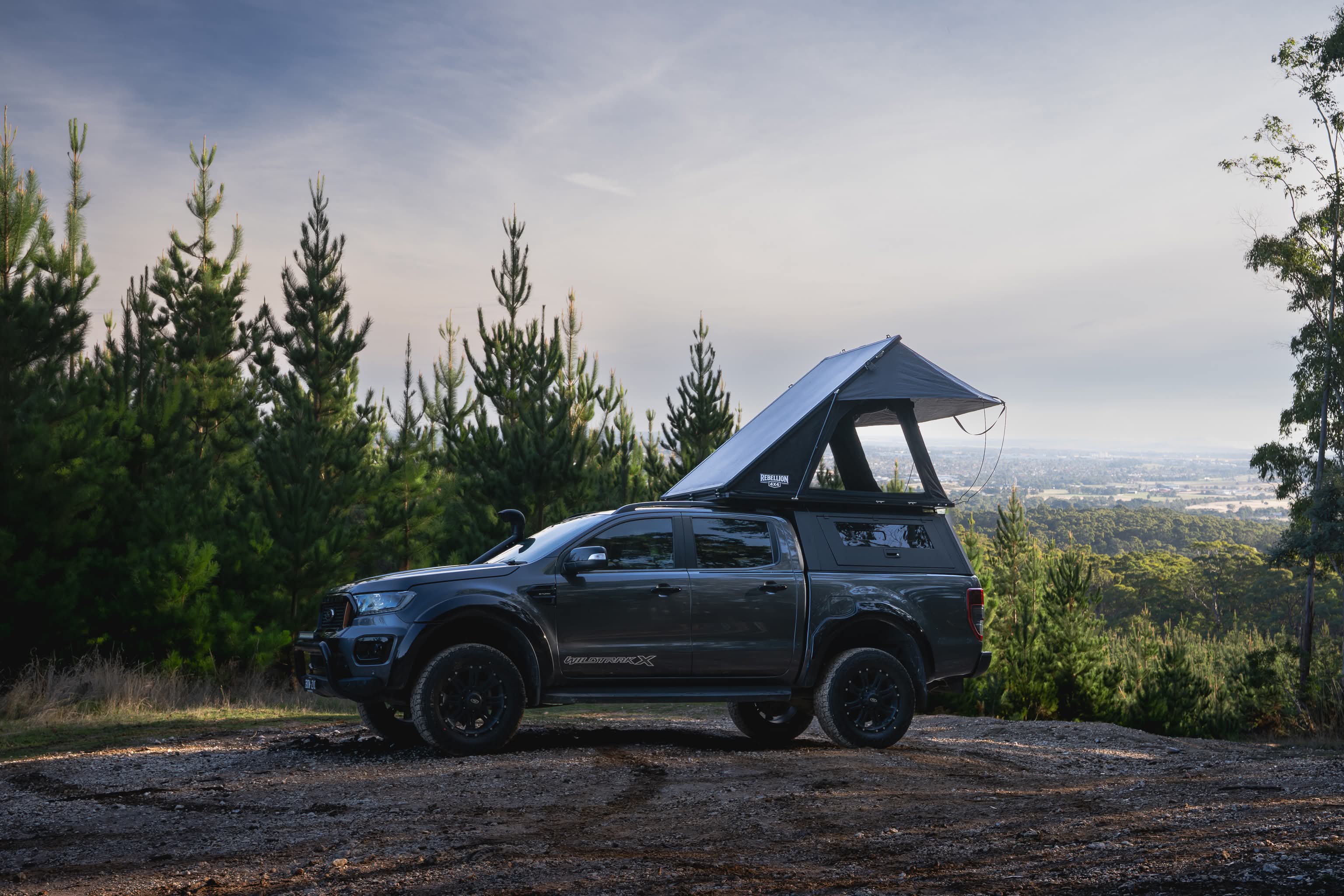 Suv with a rooftop tent parked on a dirt road surrounded by trees