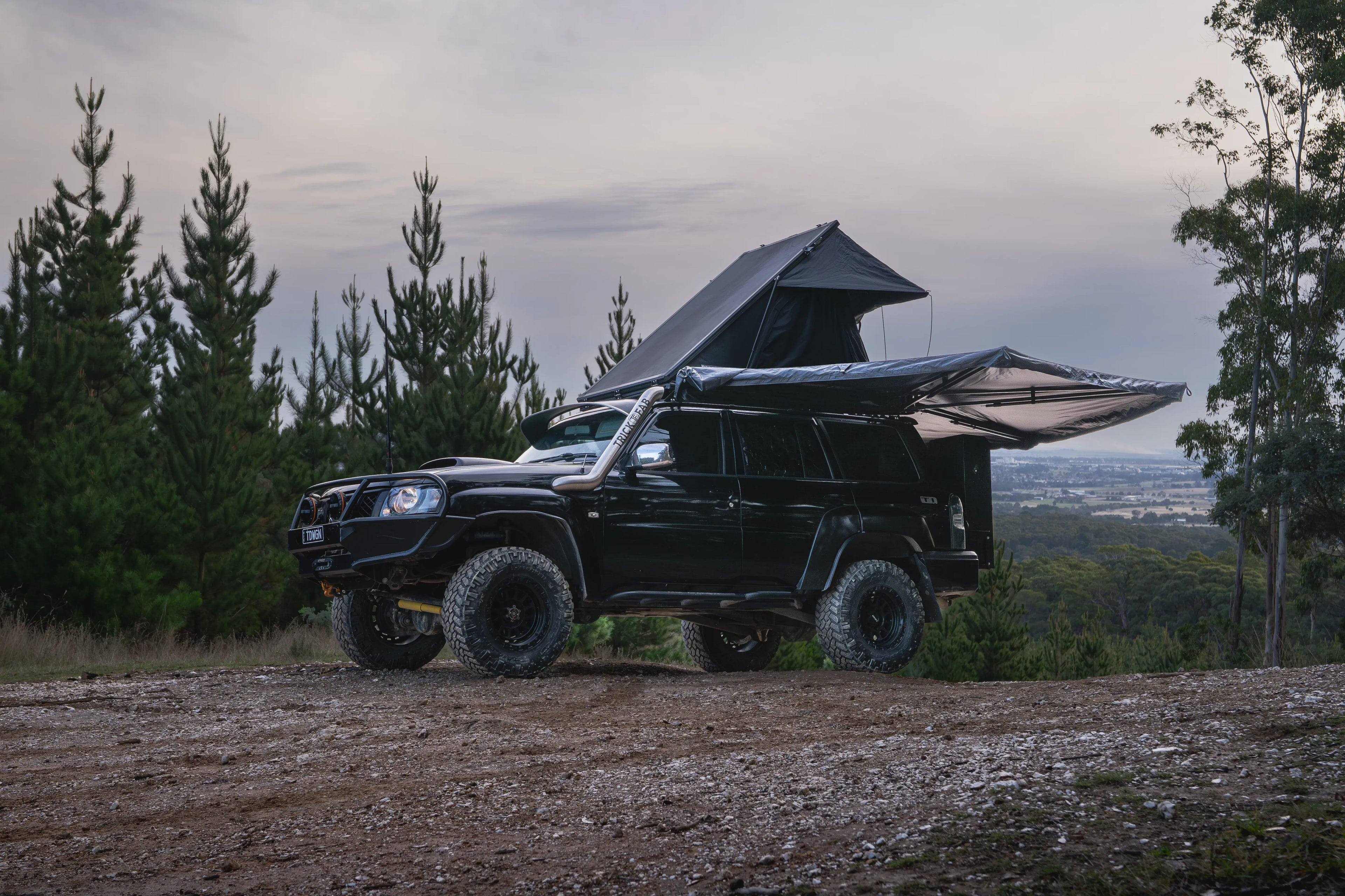 Black off-road vehicle with a roof tent parked in a forested area.
