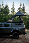 Gray truck with a rooftop tent parked in a forested area