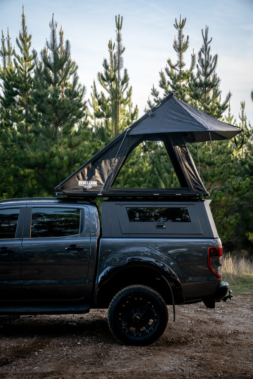 Gray truck with a rooftop tent parked in a forested area