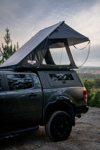 Black truck with a rooftop tent parked outdoors with a scenic background