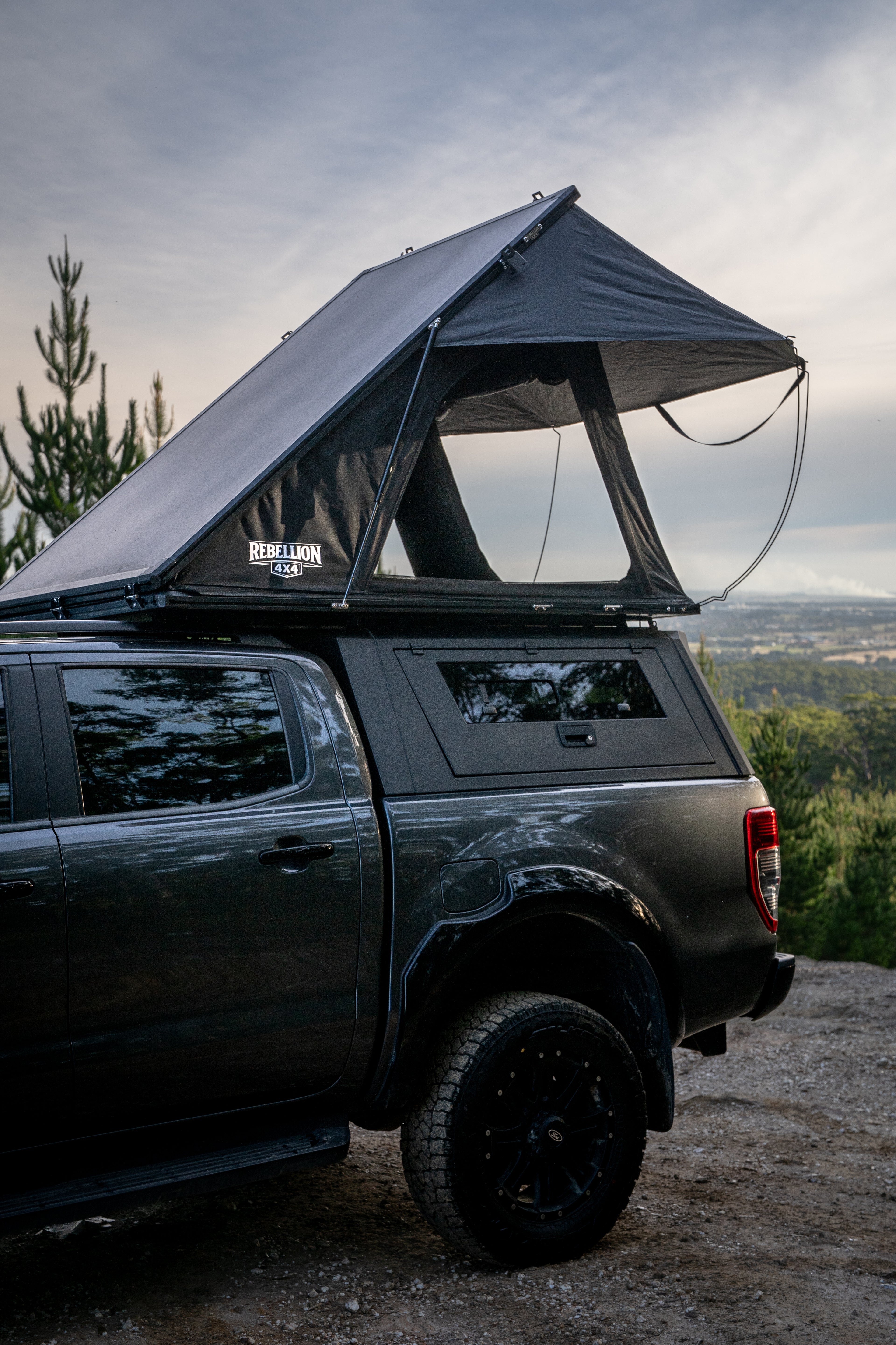 Black truck with a rooftop tent parked outdoors with a scenic background