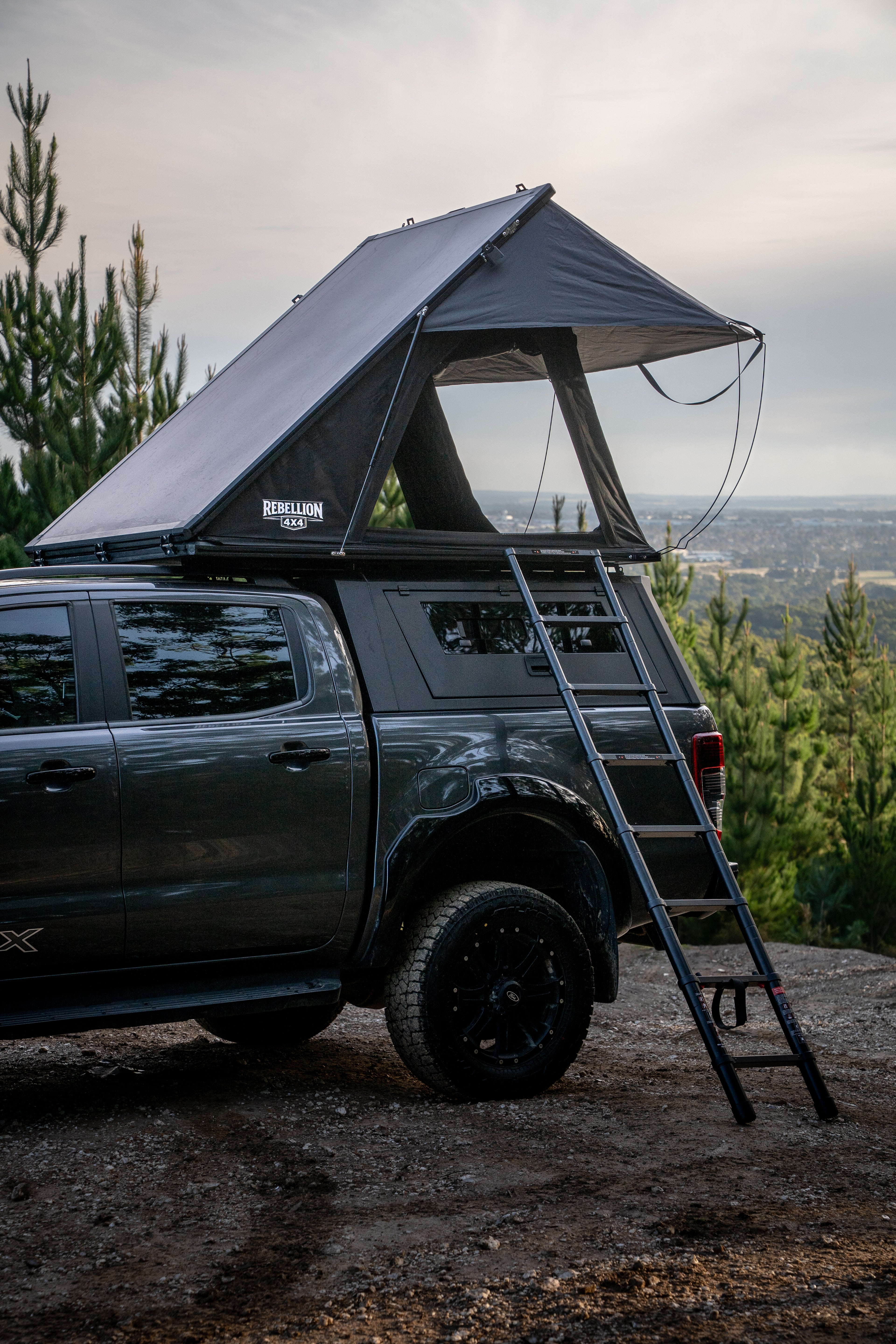 Black SUV with a rooftop tent and ladder in a forest setting