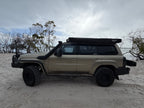 Beige Nissan Patrol parked on Sandy beach with cloudy skies with black awning
