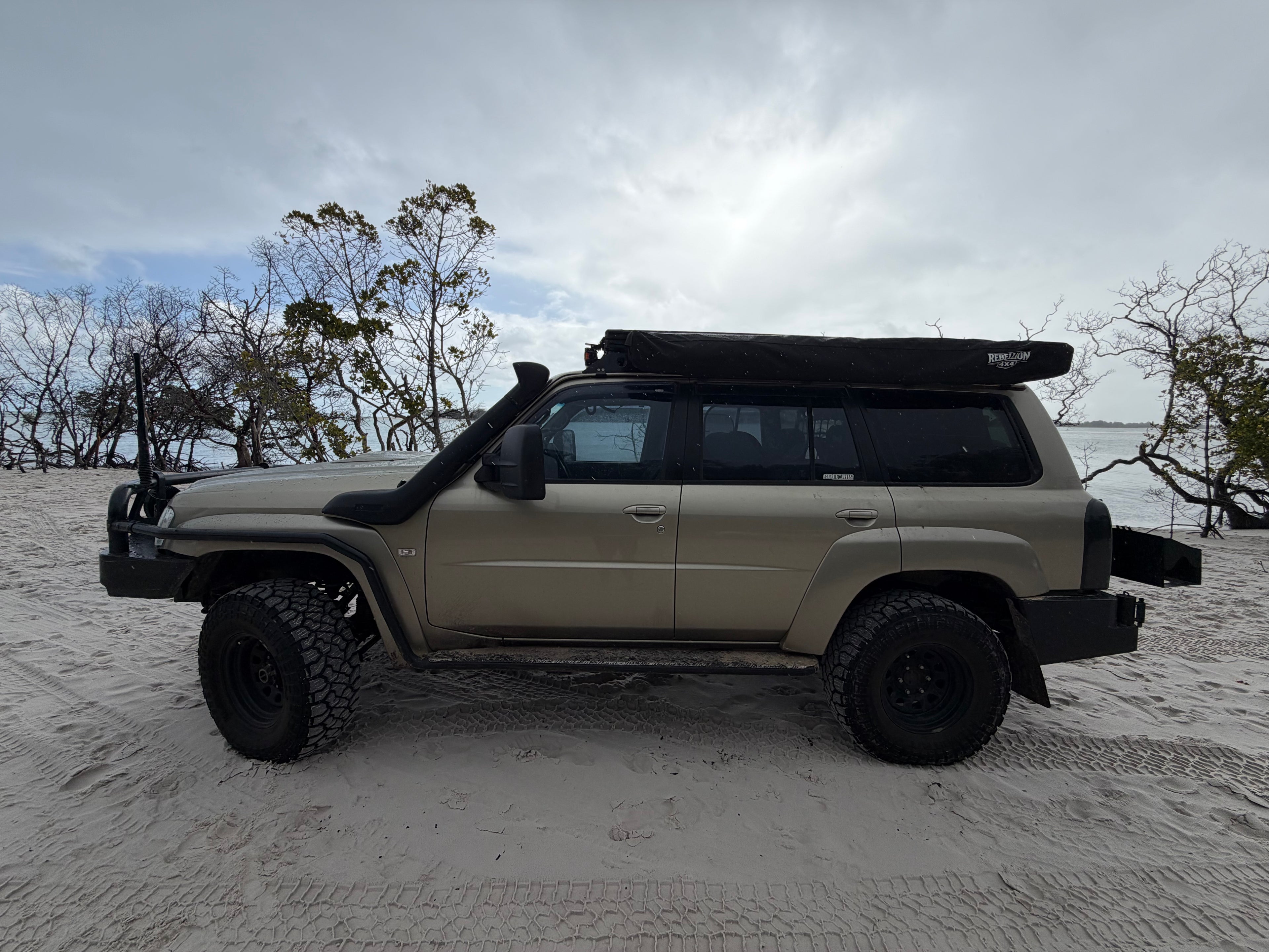 Beige Nissan Patrol parked on Sandy beach with cloudy skies with black awning